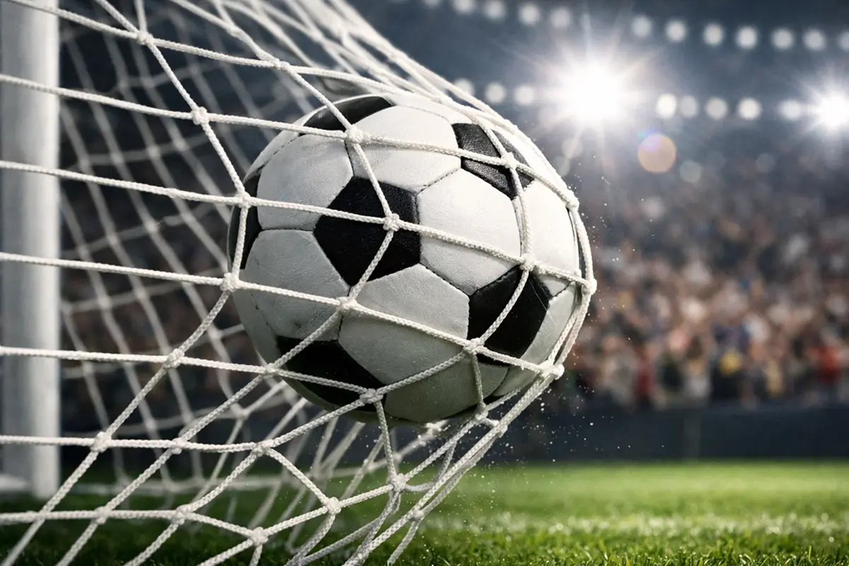Balón de fútbol entrando en la red de una portería sobre césped verde bajo focos del estadio